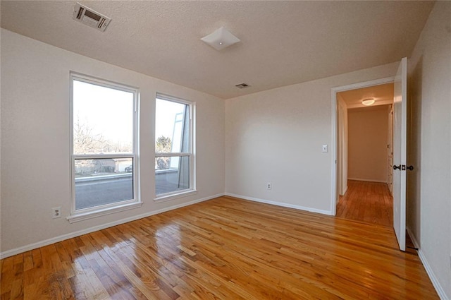 empty room with a textured ceiling and light hardwood / wood-style flooring