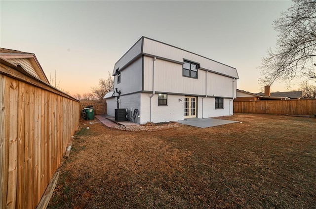 back house at dusk with central AC unit, a yard, a patio, and french doors