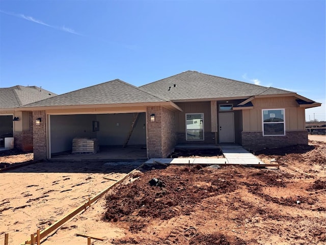 view of front of property featuring an attached garage, brick siding, and roof with shingles