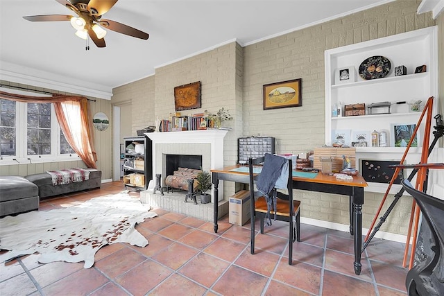 interior space featuring tile patterned floors, crown molding, a brick fireplace, ceiling fan, and brick wall