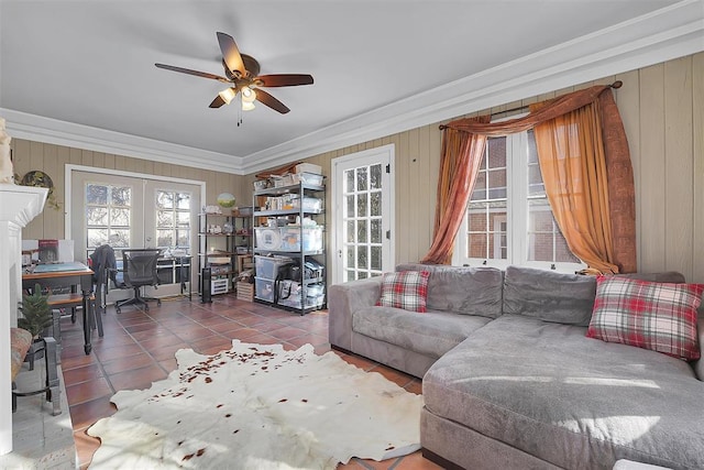 tiled living room with ornamental molding, french doors, ceiling fan, and wood walls