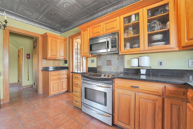 kitchen featuring stainless steel appliances, tasteful backsplash, dark stone countertops, and light tile patterned floors