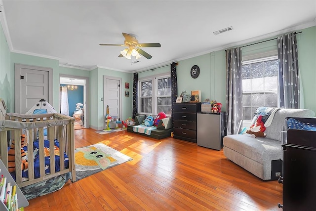 bedroom with crown molding, ceiling fan with notable chandelier, stainless steel refrigerator, and hardwood / wood-style flooring