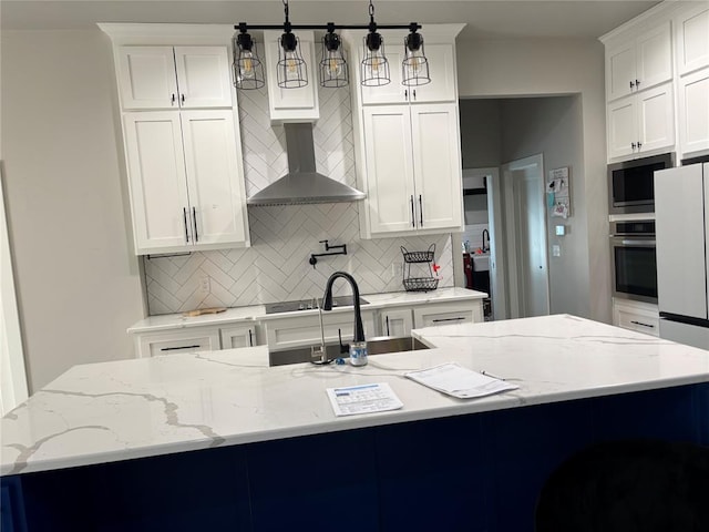 kitchen featuring hanging light fixtures, appliances with stainless steel finishes, an island with sink, and wall chimney exhaust hood