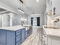 kitchen featuring decorative light fixtures, a spacious island, sink, white cabinetry, and blue cabinetry