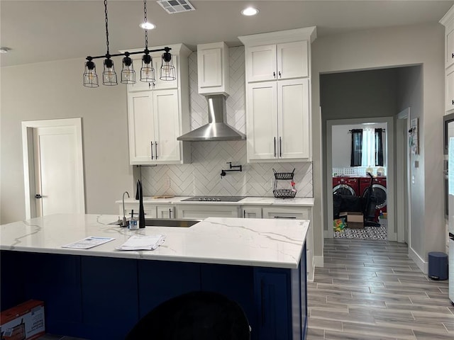 kitchen with white cabinetry, tasteful backsplash, wall chimney range hood, light stone counters, and sink