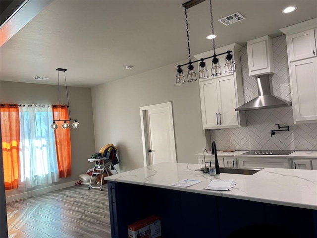 kitchen with pendant lighting, white cabinetry, wall chimney range hood, sink, and backsplash