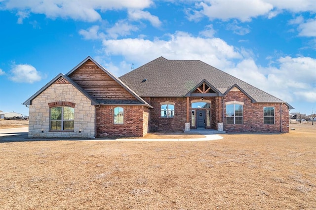 view of front facade with brick siding, a front yard, and a shingled roof