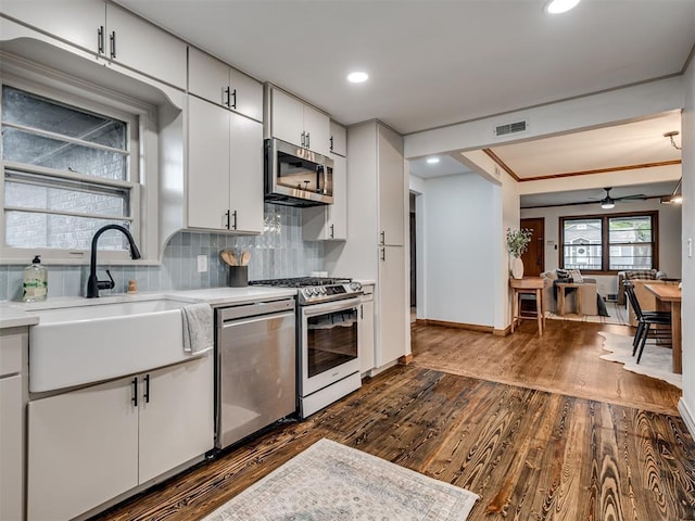 kitchen featuring dark wood-type flooring, white cabinets, ceiling fan, tasteful backsplash, and stainless steel appliances