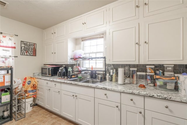 kitchen featuring backsplash, light stone counters, white cabinetry, and sink