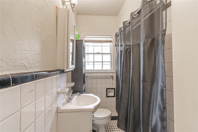 bathroom featuring walk in shower, vanity, toilet, and tile walls