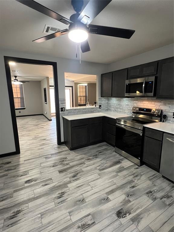 kitchen featuring ceiling fan, stainless steel appliances, light hardwood / wood-style floors, and backsplash