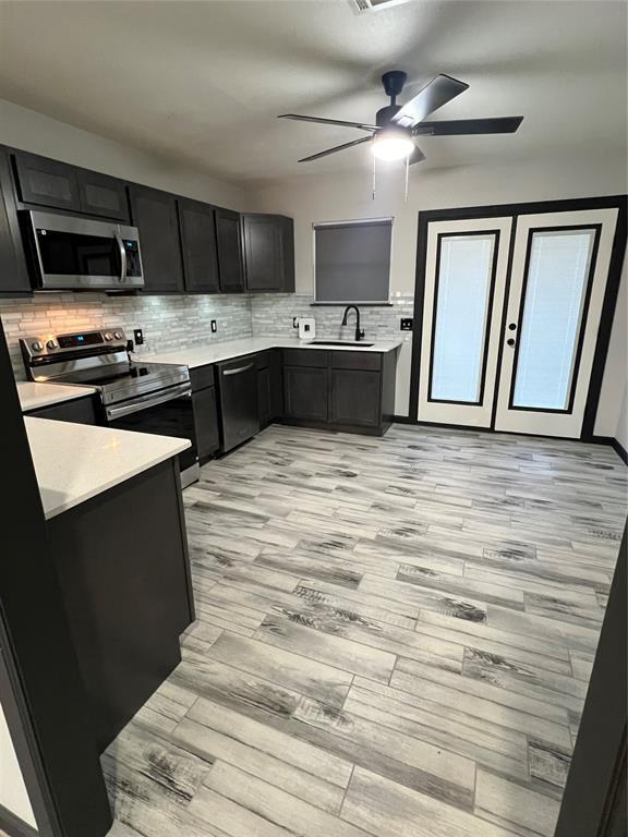 kitchen with sink, light wood-type flooring, ceiling fan, stainless steel appliances, and decorative backsplash