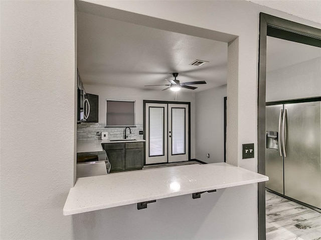 kitchen with sink, a breakfast bar area, decorative backsplash, ceiling fan, and stainless steel refrigerator with ice dispenser