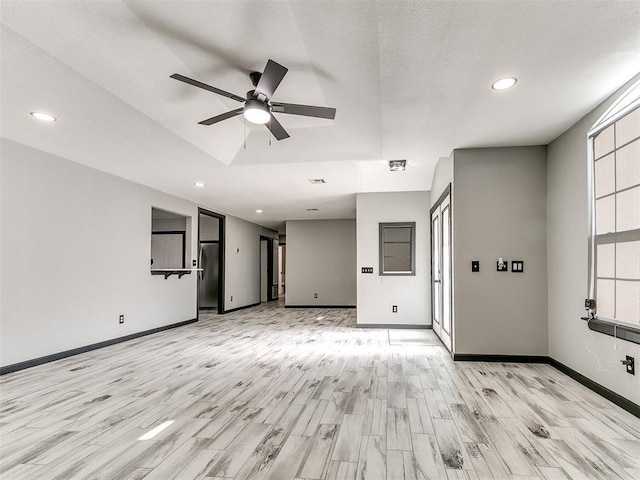 unfurnished living room featuring a tray ceiling, light hardwood / wood-style flooring, and ceiling fan