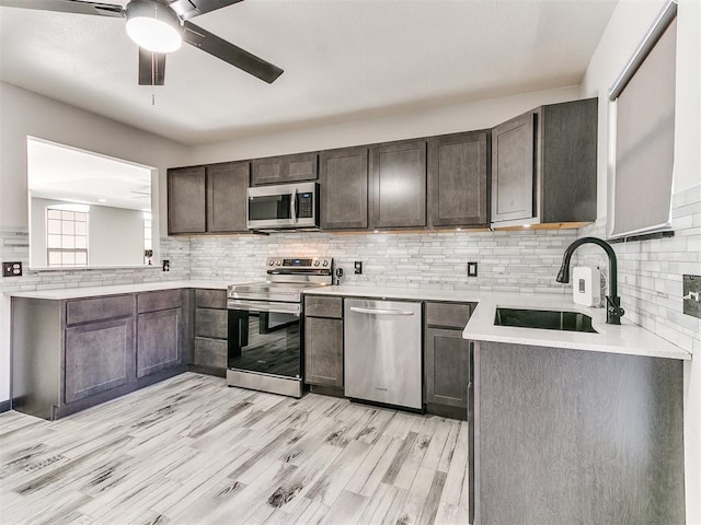 kitchen with sink, dark brown cabinets, light hardwood / wood-style flooring, appliances with stainless steel finishes, and backsplash