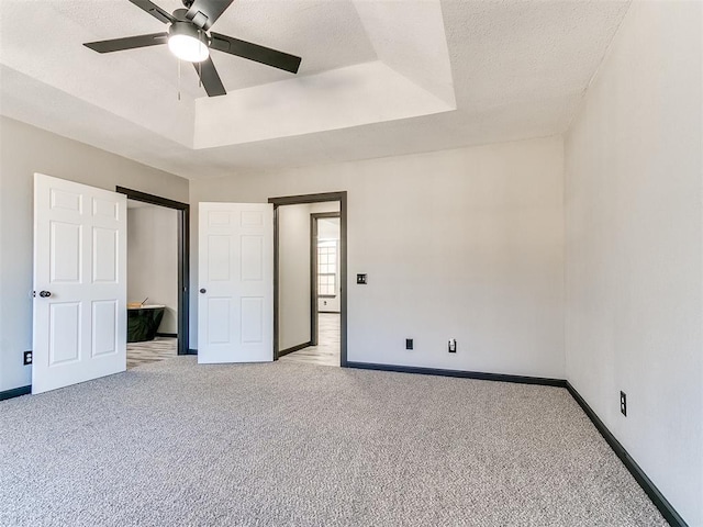 unfurnished bedroom with ceiling fan, light colored carpet, a raised ceiling, and a textured ceiling