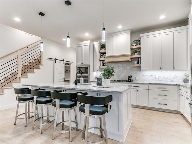 kitchen featuring built in microwave, a barn door, decorative light fixtures, a center island with sink, and white cabinetry