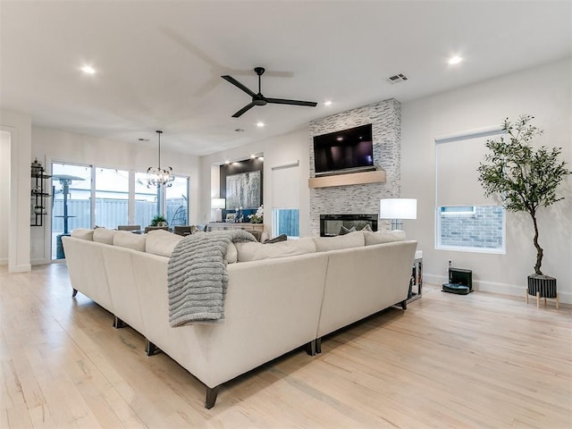 living room featuring a stone fireplace, light hardwood / wood-style flooring, and ceiling fan with notable chandelier