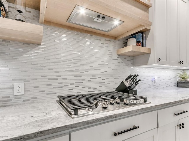 kitchen featuring white cabinets, stainless steel gas stovetop, light stone counters, and backsplash