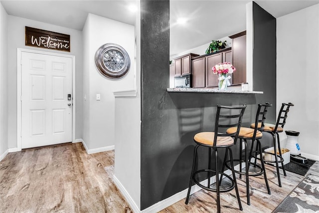 kitchen with dark brown cabinetry, light wood-type flooring, black microwave, a peninsula, and a kitchen bar