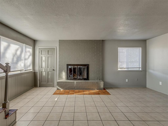 unfurnished living room with a textured ceiling, a fireplace, light tile patterned flooring, and plenty of natural light