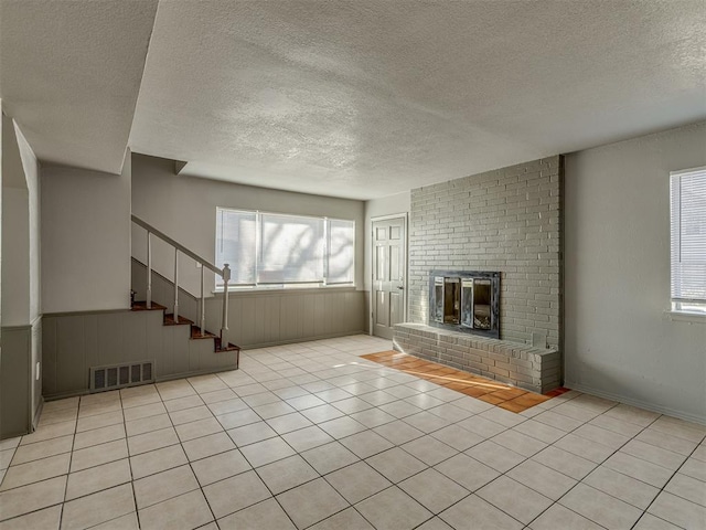 unfurnished living room with light tile patterned floors, a textured ceiling, and a brick fireplace