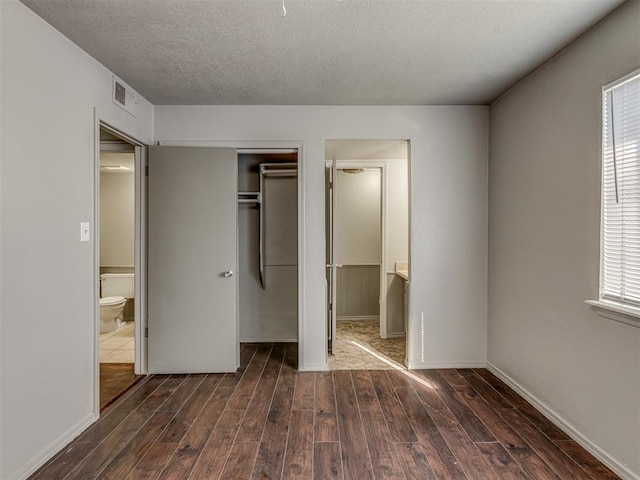 unfurnished bedroom with connected bathroom, dark wood-type flooring, and a textured ceiling