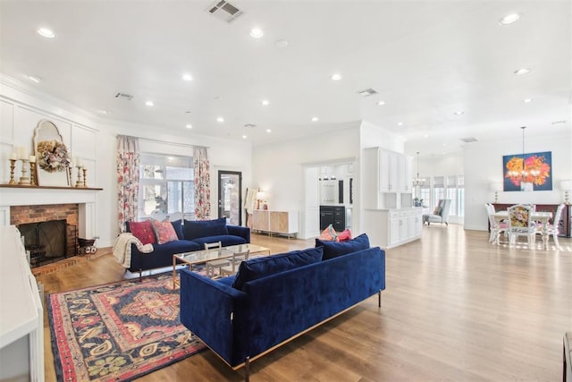 living room with ornamental molding, a brick fireplace, and light hardwood / wood-style flooring