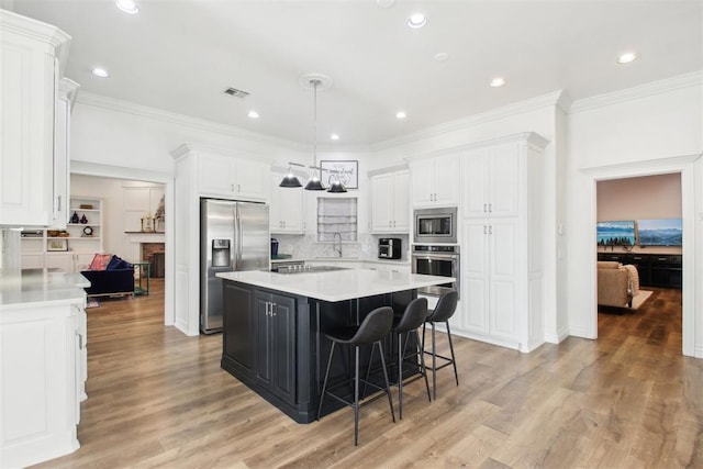 kitchen with a kitchen island, appliances with stainless steel finishes, tasteful backsplash, white cabinetry, and a kitchen bar