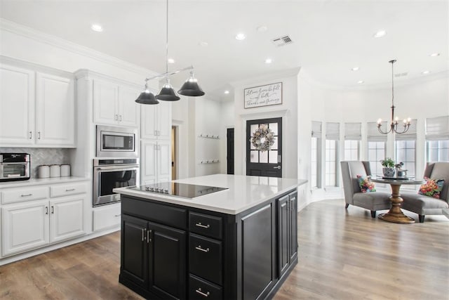 kitchen featuring hanging light fixtures, a kitchen island, white cabinets, stainless steel appliances, and backsplash