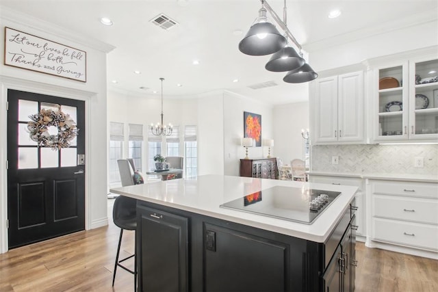 kitchen with white cabinetry, black electric stovetop, a notable chandelier, light hardwood / wood-style floors, and a kitchen island