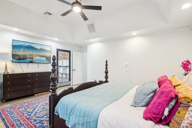 bedroom with ceiling fan, a tray ceiling, and light hardwood / wood-style flooring