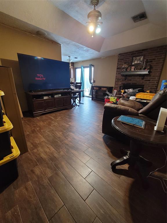 living room with a raised ceiling, ceiling fan, dark hardwood / wood-style flooring, a fireplace, and a textured ceiling