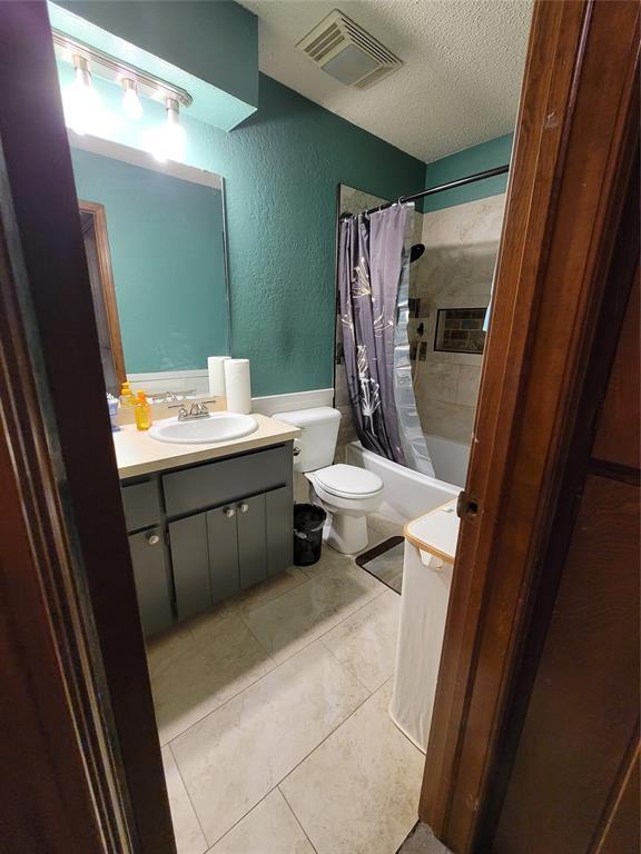 full bathroom with shower / tub combo, tile patterned flooring, toilet, vanity, and a textured ceiling