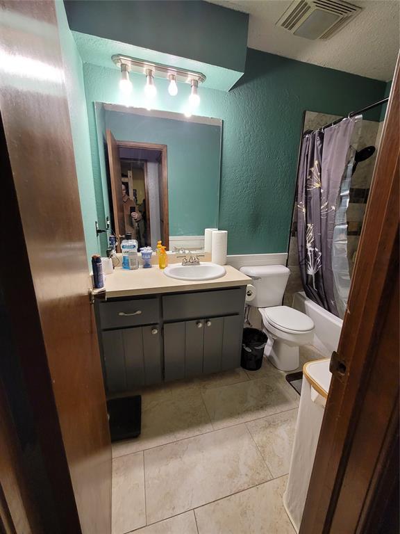 full bathroom featuring shower / bathtub combination with curtain, toilet, tile patterned floors, vanity, and a textured ceiling