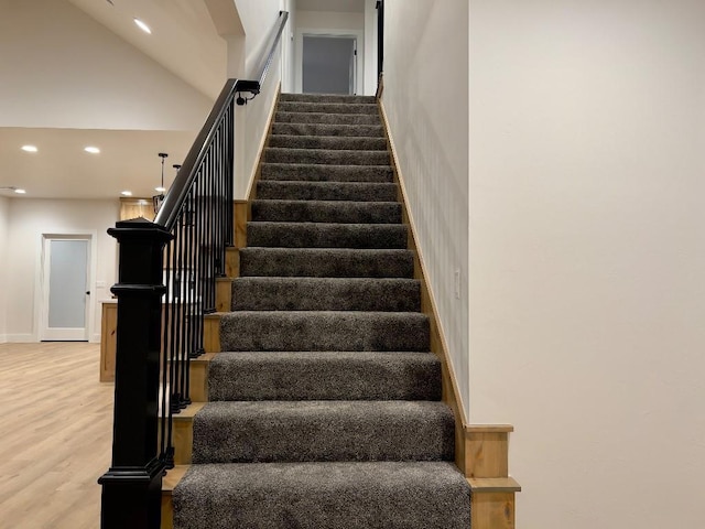 stairway featuring baseboards, high vaulted ceiling, wood finished floors, and recessed lighting