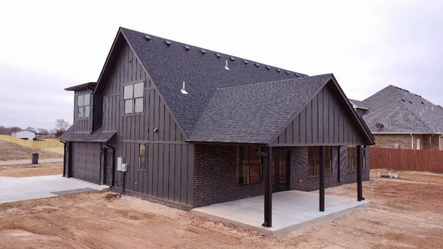 exterior space featuring a garage, a shingled roof, concrete driveway, board and batten siding, and brick siding