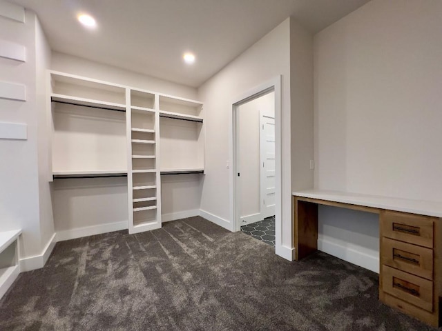 spacious closet with dark colored carpet and built in desk