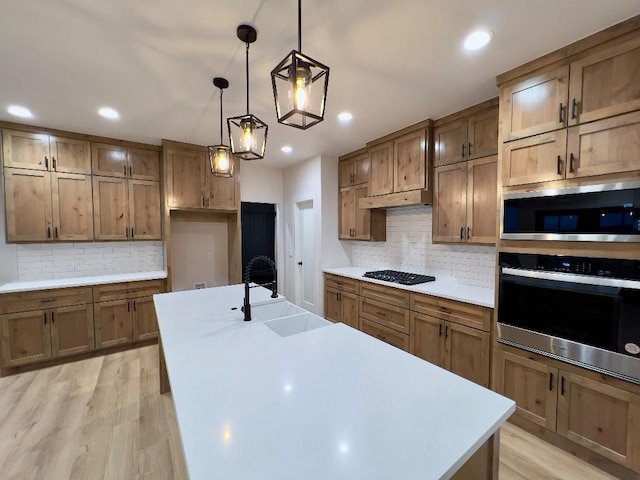 kitchen featuring appliances with stainless steel finishes, a kitchen island with sink, light countertops, light wood-style floors, and a sink