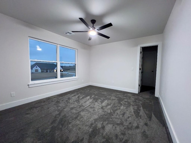 empty room featuring ceiling fan, dark carpet, visible vents, and baseboards