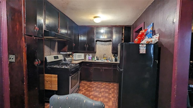 kitchen featuring white microwave, stainless steel gas range oven, under cabinet range hood, a sink, and freestanding refrigerator