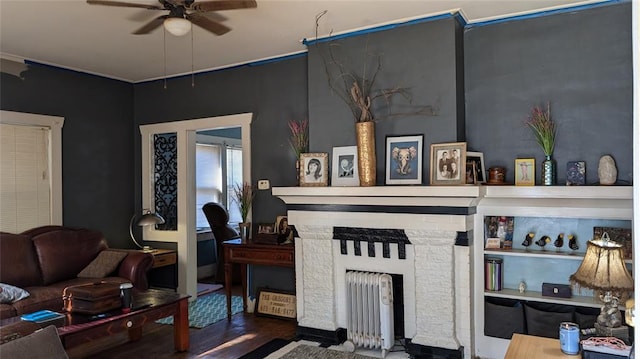 living area featuring a ceiling fan, radiator, a brick fireplace, and wood finished floors