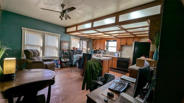 kitchen with brown cabinetry, a ceiling fan, freestanding refrigerator, light countertops, and light wood-style floors