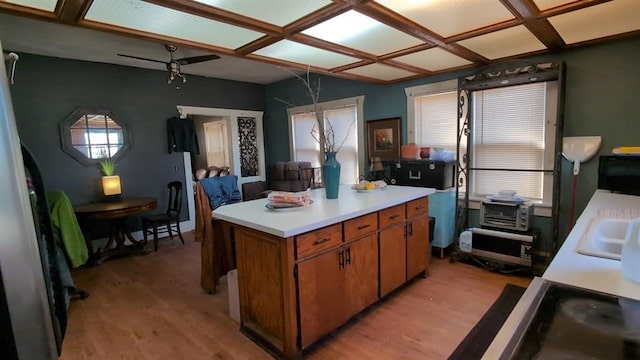 kitchen featuring light wood finished floors, brown cabinetry, a center island, light countertops, and a sink