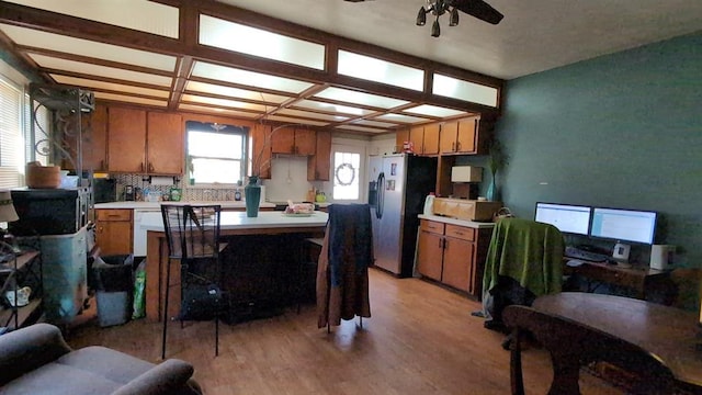 kitchen with light countertops, brown cabinetry, light wood-style floors, coffered ceiling, and stainless steel fridge with ice dispenser