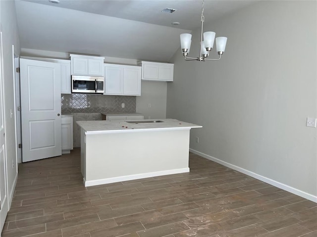 kitchen with visible vents, stainless steel microwave, backsplash, white cabinetry, and wood finished floors