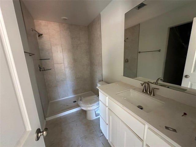 bathroom featuring toilet, tile patterned floors, a tile shower, and vanity