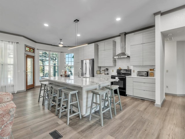 kitchen featuring ceiling fan, wall chimney range hood, black electric range, stainless steel fridge, and a spacious island