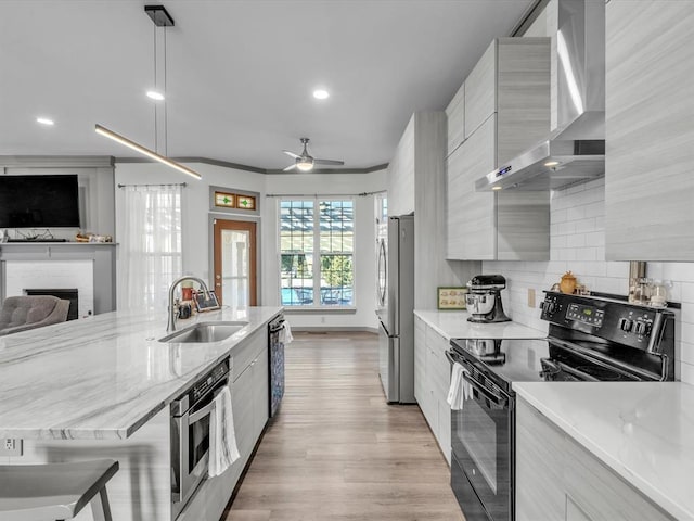 kitchen with pendant lighting, wall chimney range hood, sink, ceiling fan, and stainless steel appliances